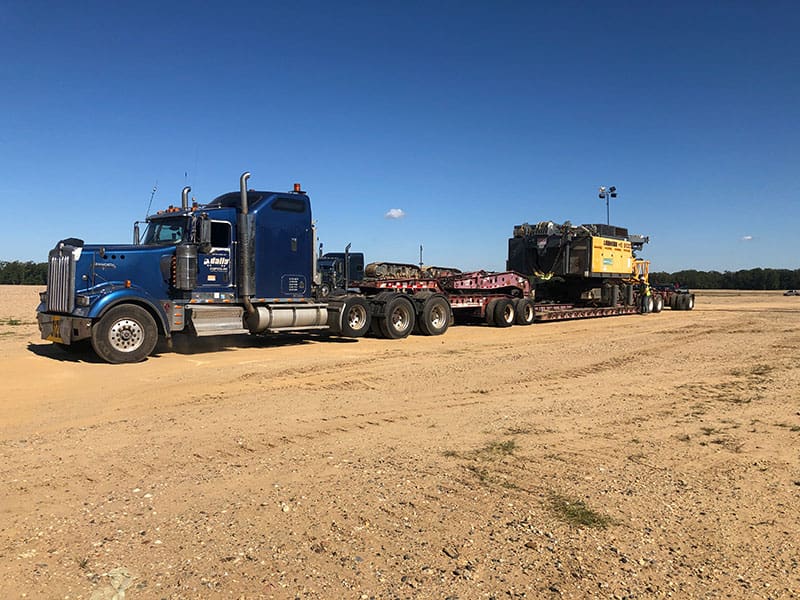 Heavy haul truck transporting large dynamic compaction crane components across a sandy construction site for ground improvement operations.