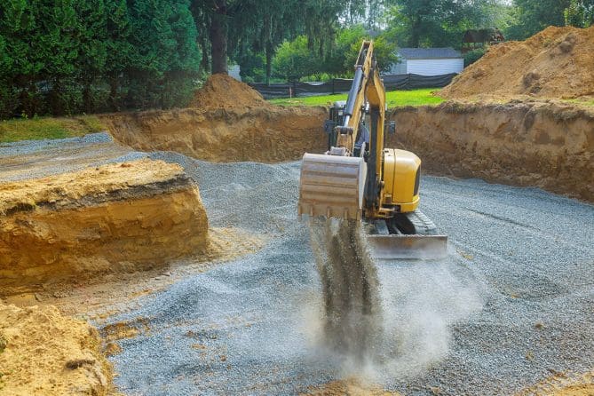 Excavator bucket scooping gravel from a construction site trench, showcasing excavation work for foundation or utility installation.