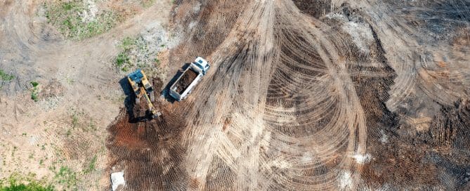 Construction site featuring a dynamic compaction crane mid-drop, with layered soil patterns and safety fencing, illustrating heavy ground improvement operations.