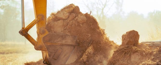 Excavator bucket lifting dry soil at a construction site, illustrating ground conditions relevant for soil densification and site preparation.