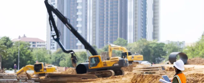 Construction site with heavy excavation equipment and cranes performing ground improvement work, while an engineer reviews plans in the foreground.