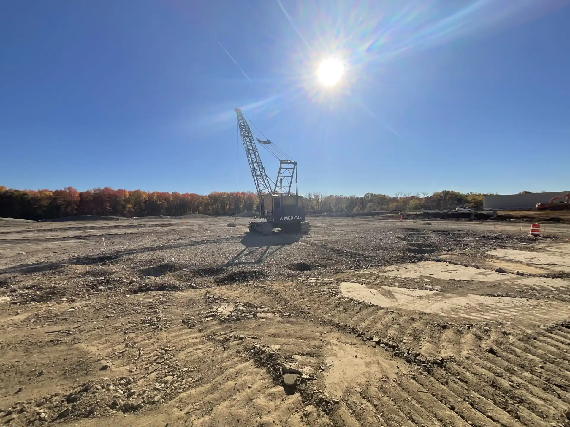 dynamic-compaction-crane-impact-craters-densification. American crawler crane performing dynamic compaction on a cleared construction site with visible impact craters