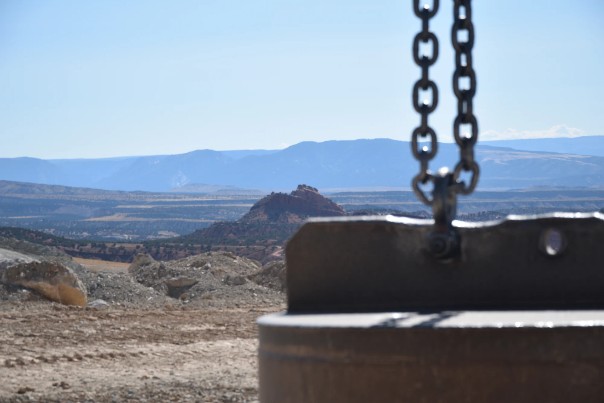 dynamic-compaction-tamper-weight-mountain-site-densification. Dynamic compaction tamper weight suspended from crane chains above a high-desert ground improvement site