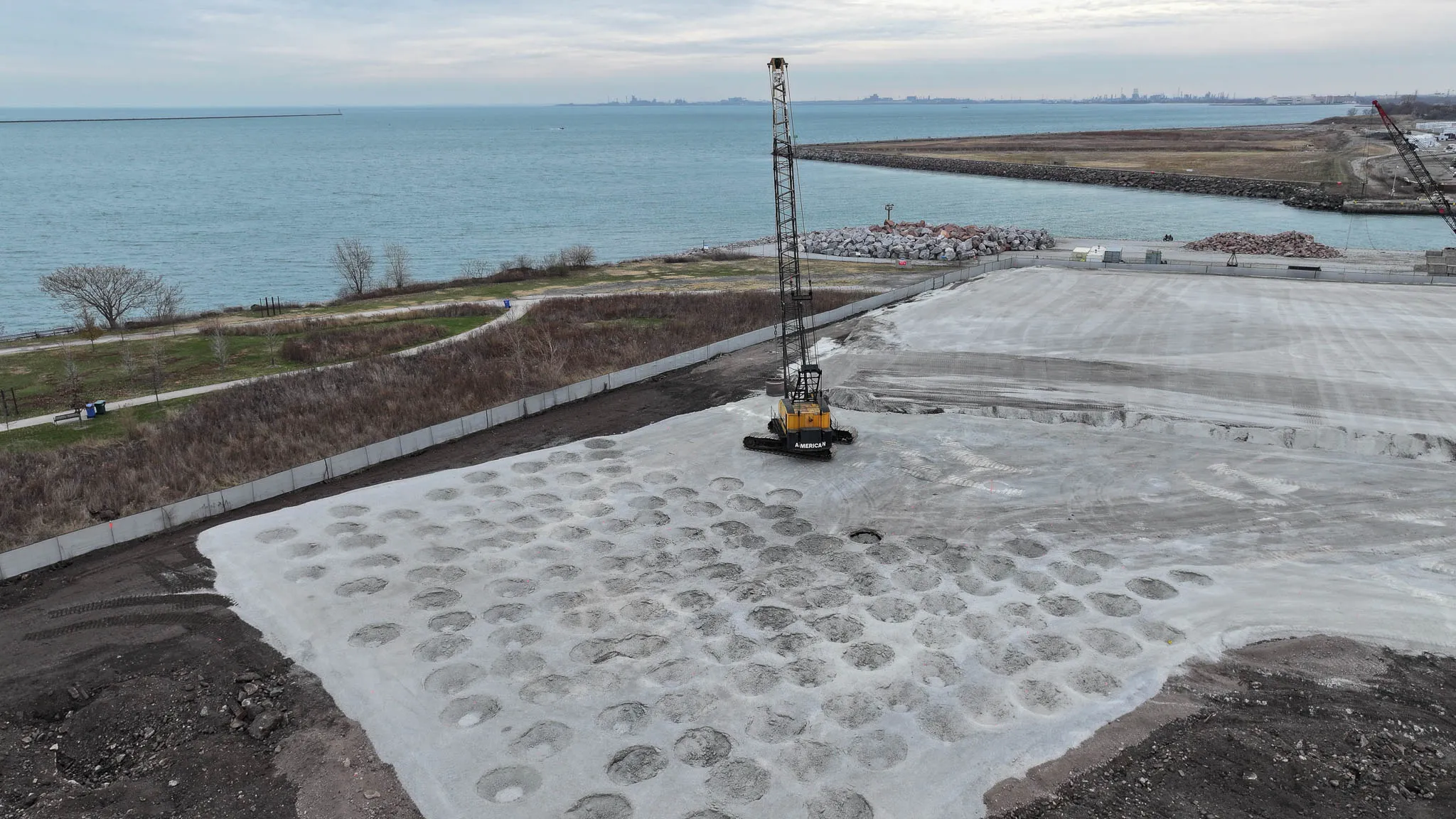 lakefront-compaction-grid-aerial-chicago-densification. American crawler crane on a lakefront pad in Chicago surrounded by a grid of dynamic compaction craters