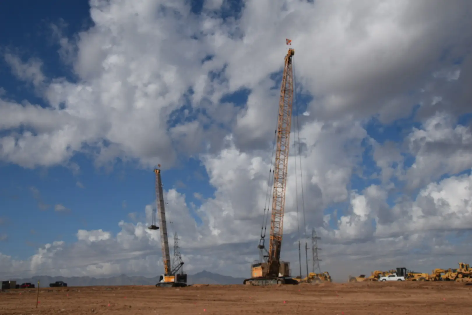 liebherr-hs8100-crawler-cranes-dynamic-compaction-densification. Two Liebherr HS8100 crawler cranes performing dynamic compaction under a dramatic sky