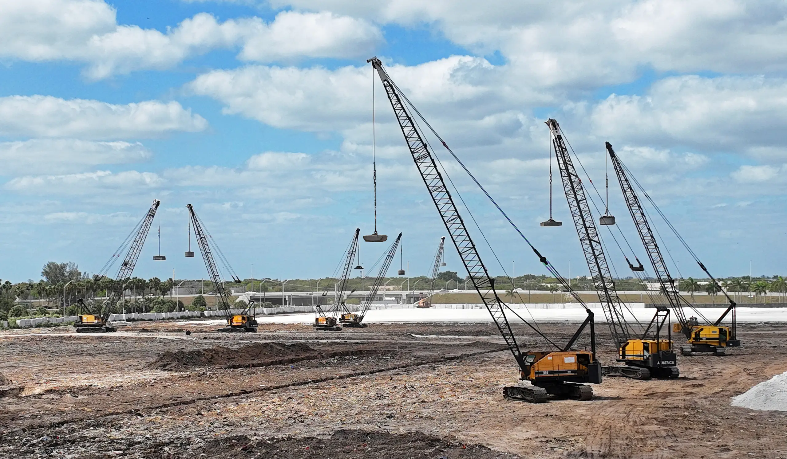 crawler-crane-fleet-staged-on-site-densification. Multiple lattice-boom crawler cranes staged across a project site, part of the Densification dynamic compaction fleet