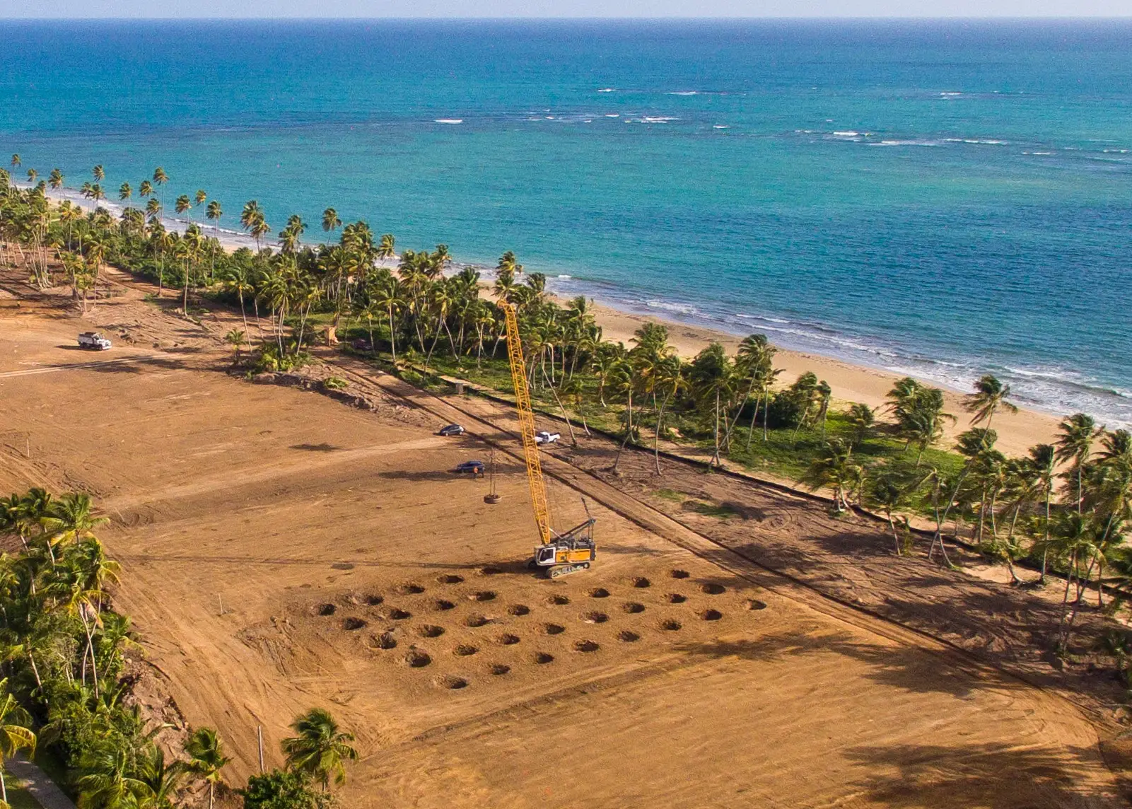 coastal-dynamic-compaction-puerto-rico-densification. Aerial view of a dynamic compaction crater grid on a coastal Puerto Rico site beside palm trees and open water