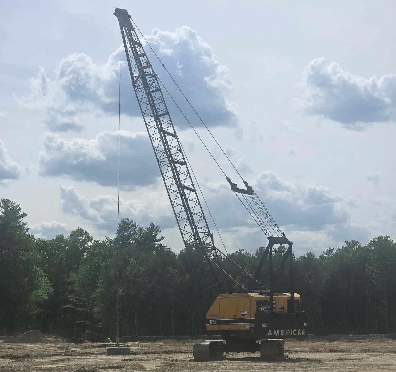 american-t250-crane-sandy-site-middleborough-densification. American T250 crawler crane with counterweights set on a sandy compaction site edged by New England pines