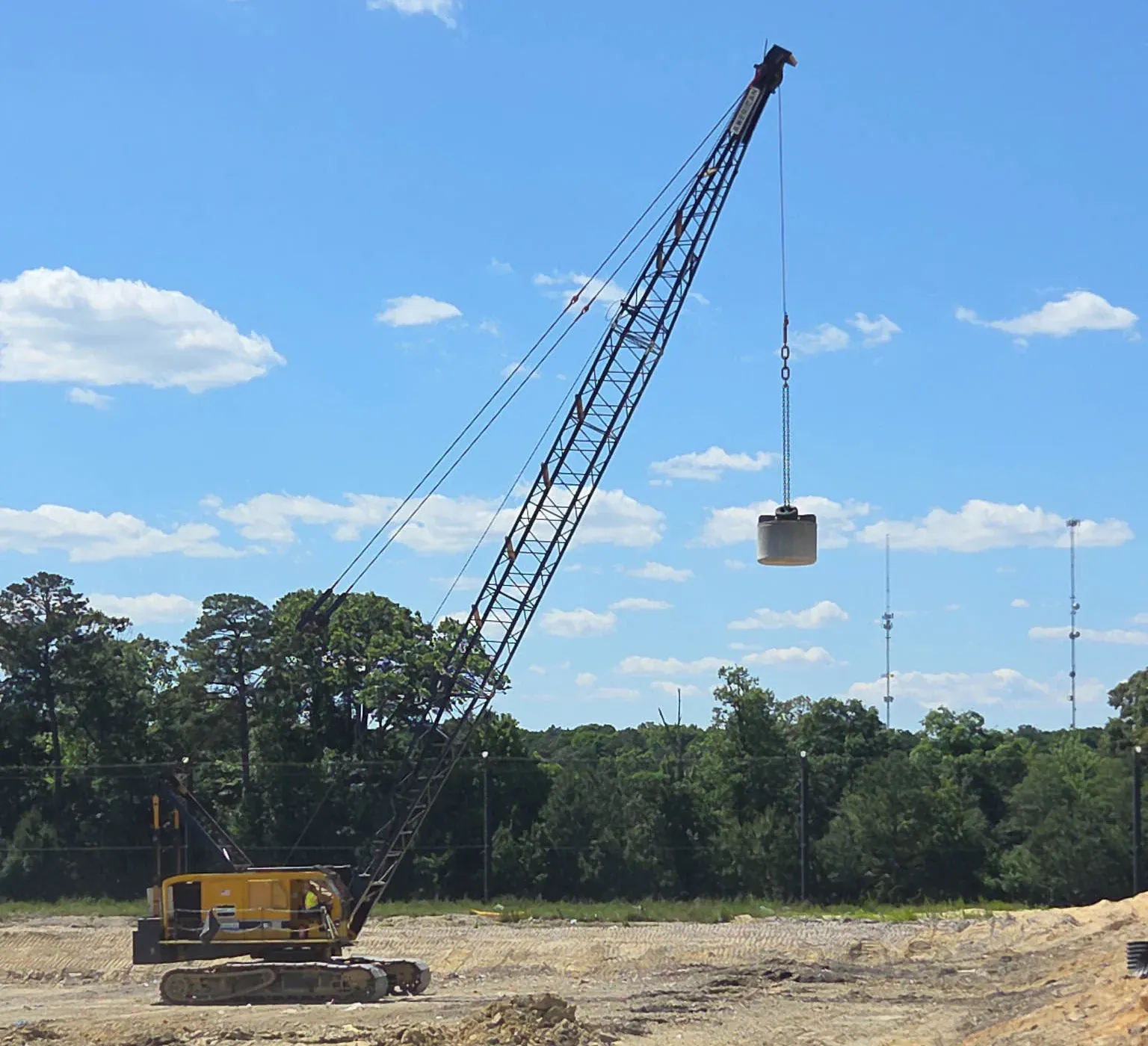 landfill-cell-compaction-salisbury-maryland-densification. Yellow crawler crane lifting a cylindrical tamper over a landfill cell under construction in Salisbury, Maryland