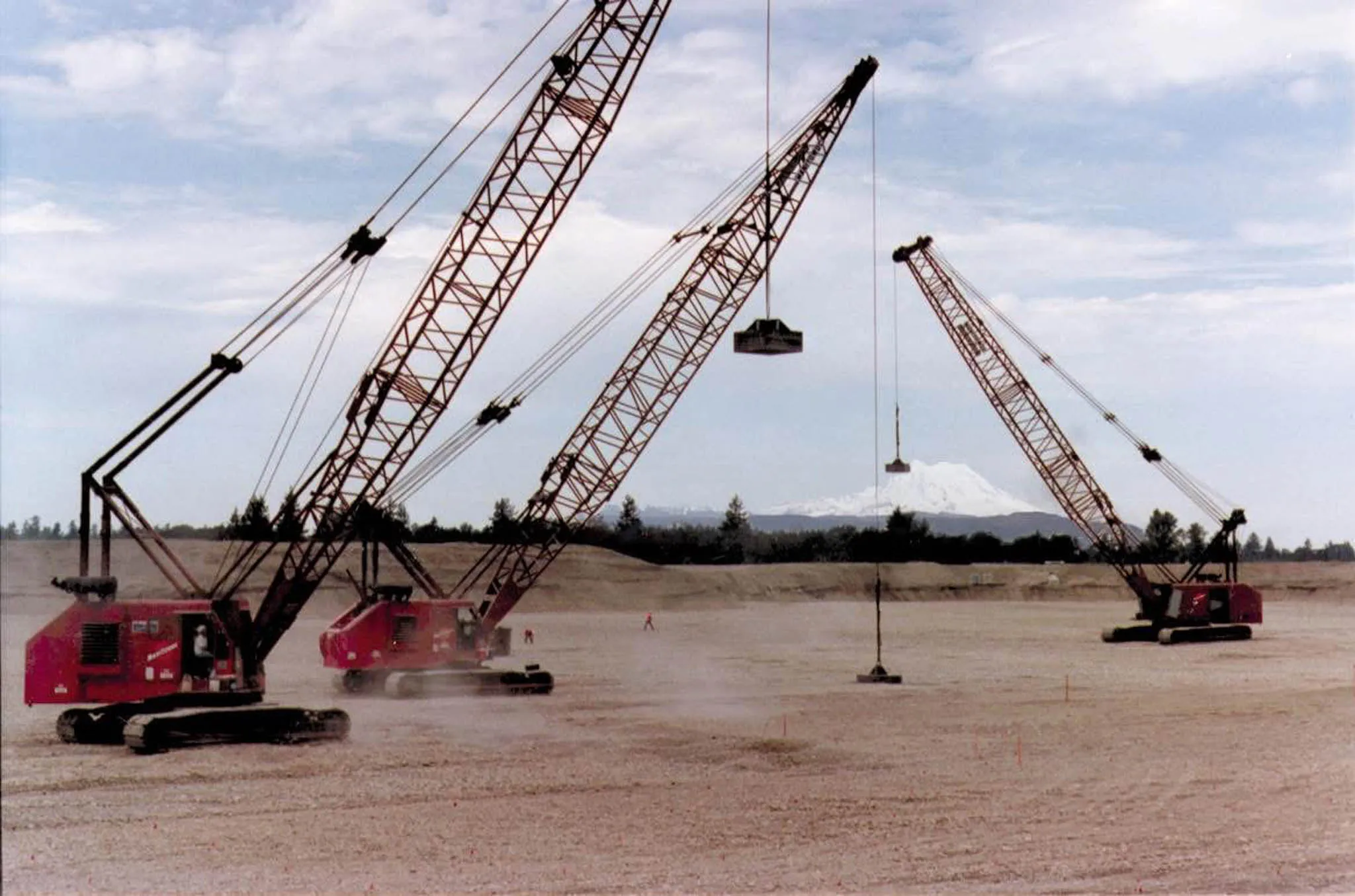three-cranes-compaction-mount-rainier-tacoma-densification. Three red Manitowoc crawler cranes running dynamic compaction near Tacoma with Mount Rainier behind