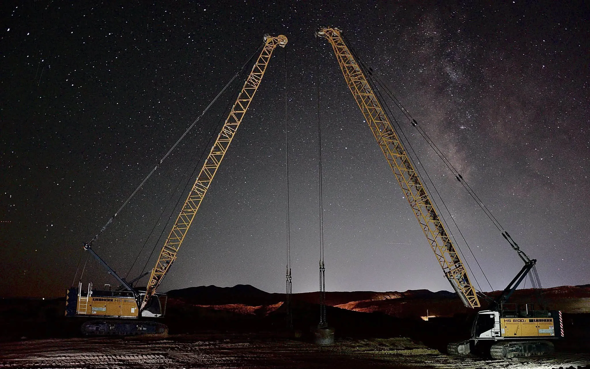 two-crawler-cranes-night-sky-vernal-utah-densification. Two Liebherr crawler cranes rigged with drop weights under a star-filled night sky in Vernal, Utah